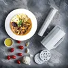 A plate of food with noodles and sauce, along with kitchen tools and ingredients, arranged on a textured gray surface. Produktbild-Vorschau