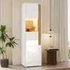 A tall, narrow display cabinet with integrated LED lighting, placed in a room setting next to a plant and a small side table. Anteprima dell’immagine prodotto