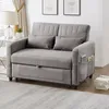 A grey sofa bed is shown in a living room setting with a lamp and pictures on the wall. Náhled obrázku produktu