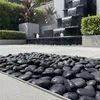 Schwarze Flusssteine vor einem modernen kaskadenartigen Gartenbrunnen Produktbild-Vorschau