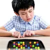 A young boy is intently playing a board game with colorful marbles. Produktbild-Vorschau