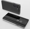 A black flip case for a smartphone is shown from two angles against a light gray background. The case has a clear front cover that displays the time. Produktbild-Vorschau