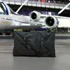 A black duffel bag is placed on the floor in front of a private jet. Podgląd zdjęcia produktu