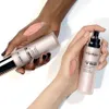 Two hands, one darker-skinned and one lighter-skinned, are holding bottles of Filorga Lift-Structure Ultra-Lifting Rosy-Glow Fluid. Swatches of the product are visible on the back of each hand. Voir les images du produit
