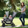 A woman pushing a double stroller with two babies in a park. Produktbild-Vorschau