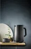 A black insulated jug is placed on a shelf next to a marble-like plate and a small bowl with a plant sprig in a vase. Voir les images du produit