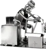 A metal sculpture of a person working on a tattoo machine, with a toolbox and a cart. Produktbild-Vorschau