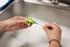 Hands cleaning a green bottle cap with a small brush in a soapy sink. Produktbild-Vorschau