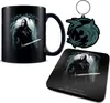 A collection of Witcher-themed merchandise including a mug, keychain, and coaster, displayed against a white background. Voir les images du produit