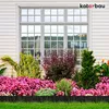 A garden bed with pink flowers and green plants bordered by a black fence in front of a house window. Voir les images du produit