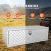 A diamond-plate aluminum truck tool box is shown in a split image. The left side shows a dry, outdoor landscape with icons highlighting features like anti-UV and scratch resistance. The right side shows a rainy, outdoor scene with a truck in the background Podgląd zdjęcia produktu