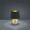 A table lamp with a black shade and a gold base is shown against a dark gray background. Náhled obrázku produktu