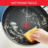 A hand is cleaning a frying pan with a sponge under running water. The pan has food residue on it. There is text overlaying the top of the image. Produktbild-Vorschau