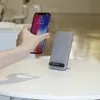 A hand holding a smartphone is about to place it on a wireless charging stand on a white table. Produktbild-Vorschau