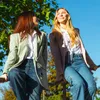 Two women sitting on a railing outdoors, looking away from the camera. Anteprima dell’immagine prodotto
