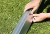 Hands assembling a metal garden edging product on grass. Produktbild-Vorschau