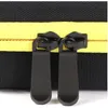 A close-up view of two black zipper pulls on a black and yellow case. Produktbild-Vorschau