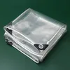 A folded clear PVC tarp with reinforced corners and grommets, laid on a green surface. Náhled obrázku produktu