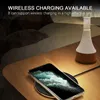 A phone is wirelessly charging on a nightstand next to a lamp, with a person sleeping in the background. Anteprima dell’immagine prodotto