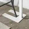 Close-up of the base of a white floor lamp and a dark metal chair leg on a concrete floor. Produktbild-Vorschau