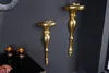Two ornate gold wall consoles are mounted on a dark gray wall, with two glass candle holders on a black surface below. Produktbild-Vorschau