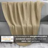 A knitted blanket draped over a sofa, with a certification logo and descriptive text overlay. Náhled obrázku produktu