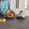 A person is holding a glass dish with a roasted chicken and vegetables, next to a Ninja CRISPi air fryer. Anteprima dell’immagine prodotto