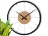 A modern wall clock with a bicycle wheel design, placed against a white background with a plant in the foreground. Produktbild-Vorschau