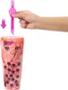 A hand is shown inserting a pink straw into a clear plastic cup filled with a pink toy. Podgląd zdjęcia produktu