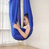 A young girl is sitting in a blue aerial hammock, looking at a tablet. Produktbild-Vorschau