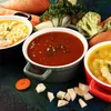 Three bowls of soup are arranged with various vegetables and root vegetables on a dark, textured surface. Náhľad obrázku produktu