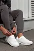 A person is sitting down and adjusting their sweatpants over white sneakers. Produktbild-Vorschau