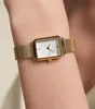 A close-up shot of a gold-toned watch with a white face on a person's wrist. Náhled obrázku produktu