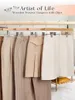 A collection of beige and cream colored trousers and skirts hanging on wooden hangers. Produktbild-Vorschau