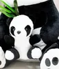 A close-up view of a large plush panda with a smaller plush panda in its lap, with some green bamboo leaves visible. Produktbild-Vorschau