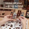Hands assembling a miniature bookshop model with instructions. Náhled obrázku produktu