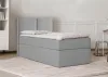 A grey bed with a headboard and bedding is shown in a room with a bookshelf and a chair in the background. Produktbild-Vorschau
