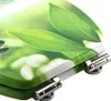 A close-up view of a toilet seat with a green leaf pattern and chrome hinges. Náhled obrázku produktu