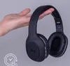 A hand holding black headphones against a light gray background. Produktbild-Vorschau