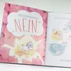 An open children's book with illustrations of unicorns. The left page shows a large unicorn in a speech bubble saying "NEIN". The right page shows smaller illustrations of unicorns in different scenarios. Voir les images du produit