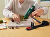A person is using a hot glue gun to craft a decorative item, possibly for Christmas, with pine cones and moss. Produktbild-Vorschau