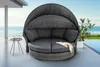 A round outdoor daybed with a canopy and cushions is placed on a deck next to a swimming pool with the ocean in the background. Produktbild-Vorschau
