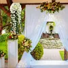 Weiße künstliche hängende Glyzinienblumen mit grünen Blättern, aufgehängt an einem Holzbalken einer Pergola Náhled obrázku produktu
