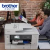 Two people are in an office setting, looking at a document near a Brother printer. Voir les images du produit