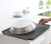 A hand is placing a pot on a dark gray dish drying rack next to a sink. Podgląd zdjęcia produktu