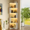 A white corner bookshelf with LED lighting is placed in a room next to a window with a view of greenery and a sofa. Voir les images du produit