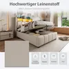 A bedroom scene featuring a bed with its storage compartment open, showcasing the mattress and bedding. The image also includes a bedside table and a window with a view. Produktbild-Vorschau