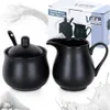 A black porcelain sugar bowl with a lid and spoon, and a black porcelain milk jug, are displayed next to a product box. Sugar granules and milk splashes are also visible. Produktbild-Vorschau