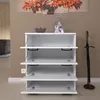 A white shoe cabinet with four open doors, displaying its interior shelves. An umbrella stand with an umbrella is to the right. A painting of autumn leaves hangs on the wall behind. Produktbild-Vorschau
