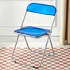 A blue transparent folding chair with a silver frame is shown in a room with a checkered floor and a white wall. Produktbild-Vorschau